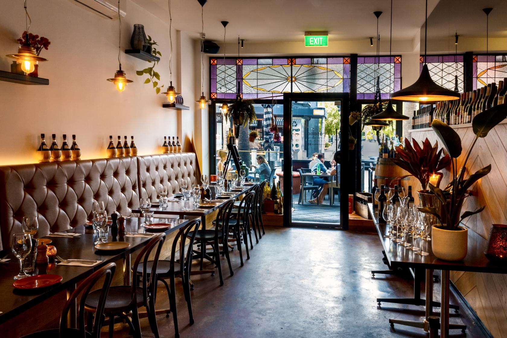 An event space with tufted banquette seating, stained glass windows, and pendant lighting at Rococo.