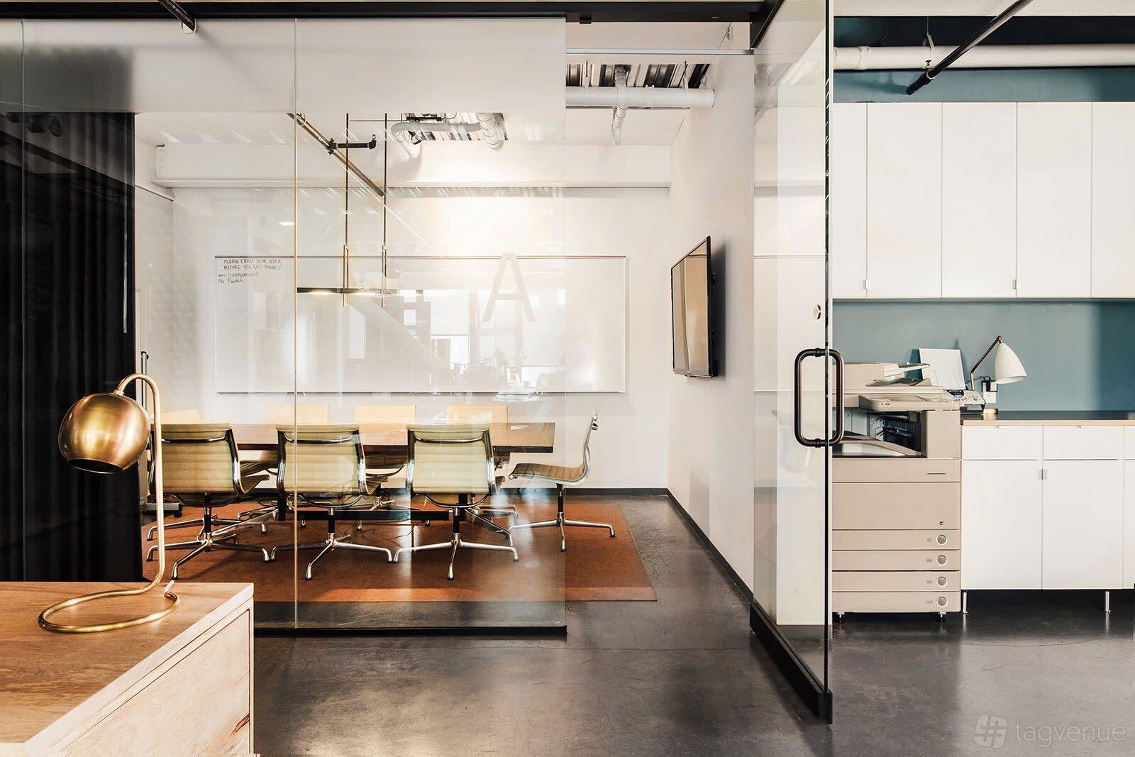 A coworking space with a glass-walled conference room, long table, rolling chairs, and wall-mounted whiteboard at The Cloud Room Coworking Space.