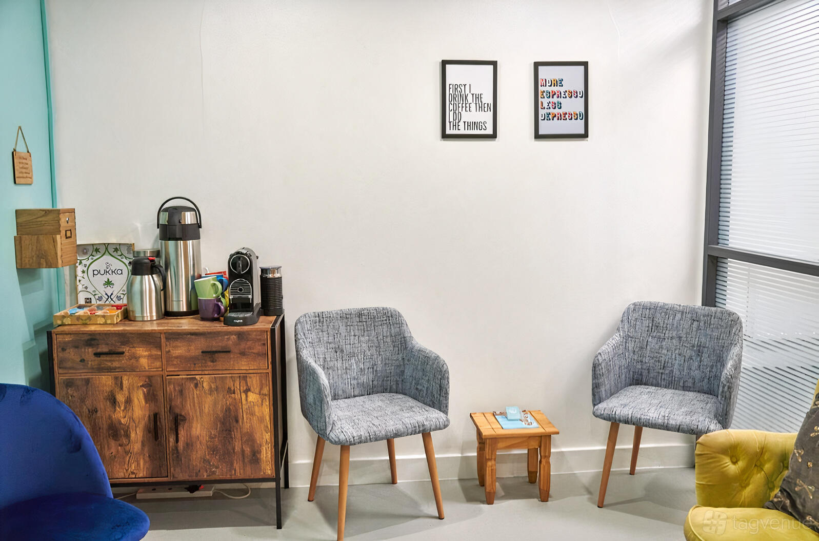 A yoga studio with cushioned chairs, a wooden cabinet with a coffee set, and framed artwork at H L Therapy.