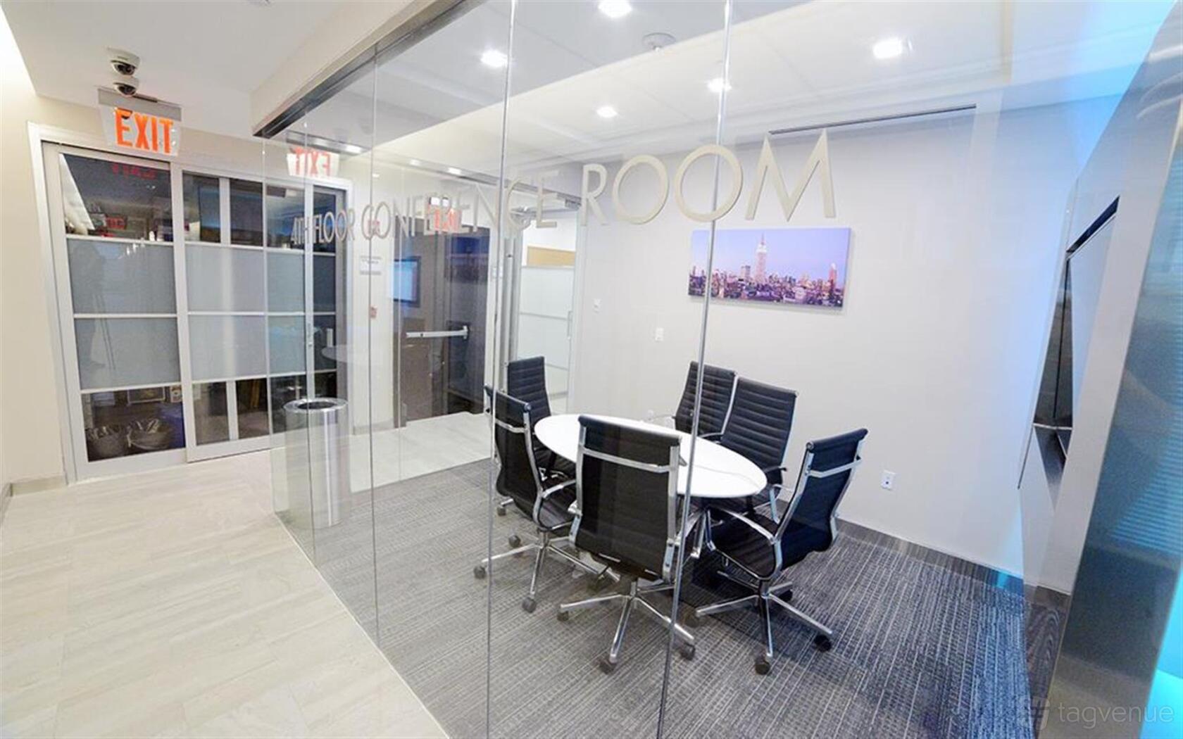 A meeting room with glass walls, round table, black leather chairs, and wall-mounted artwork at Madison Avenue Jay Suites.