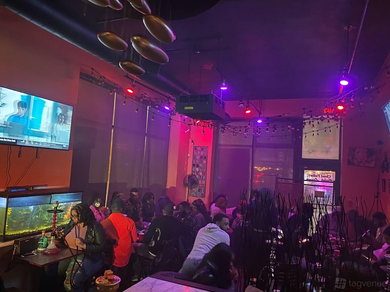A bar with colorful LED lighting, wall-mounted TVs, and a large aquarium at Cloud Factory Hookah Lounge.