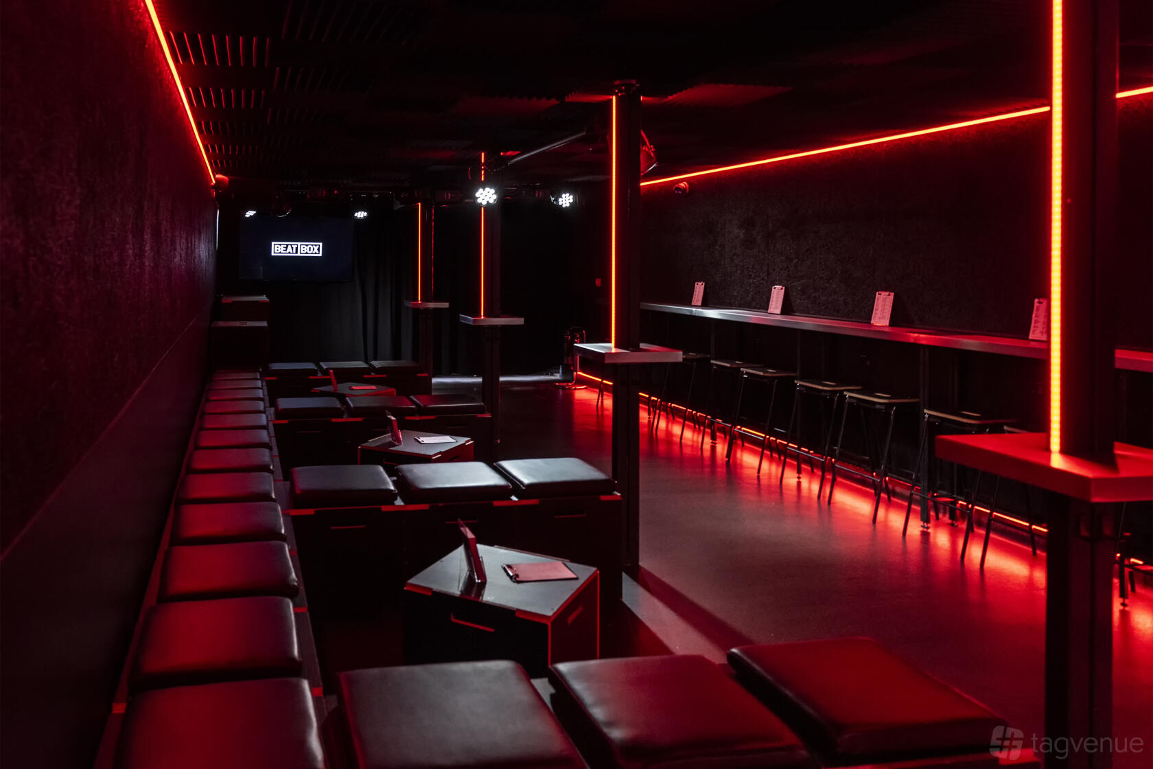 A restaurant event room with red LED lighting, black seating, and high tables with stools at Boxpark Shoreditch.