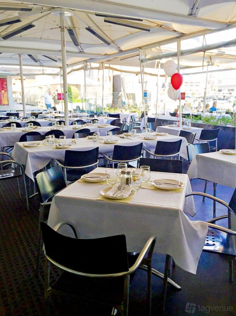 A dining room with black chairs, square tables covered in white linens, and glassware at Renzo's Bar.