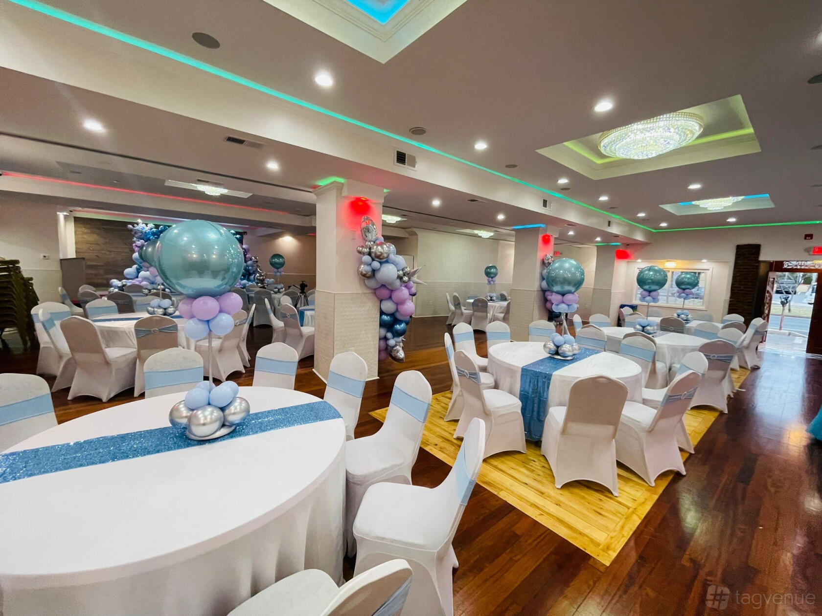 An event venue with round tables draped in white linens, pastel balloon centerpieces, and wood flooring at Dhaka Club Party center.