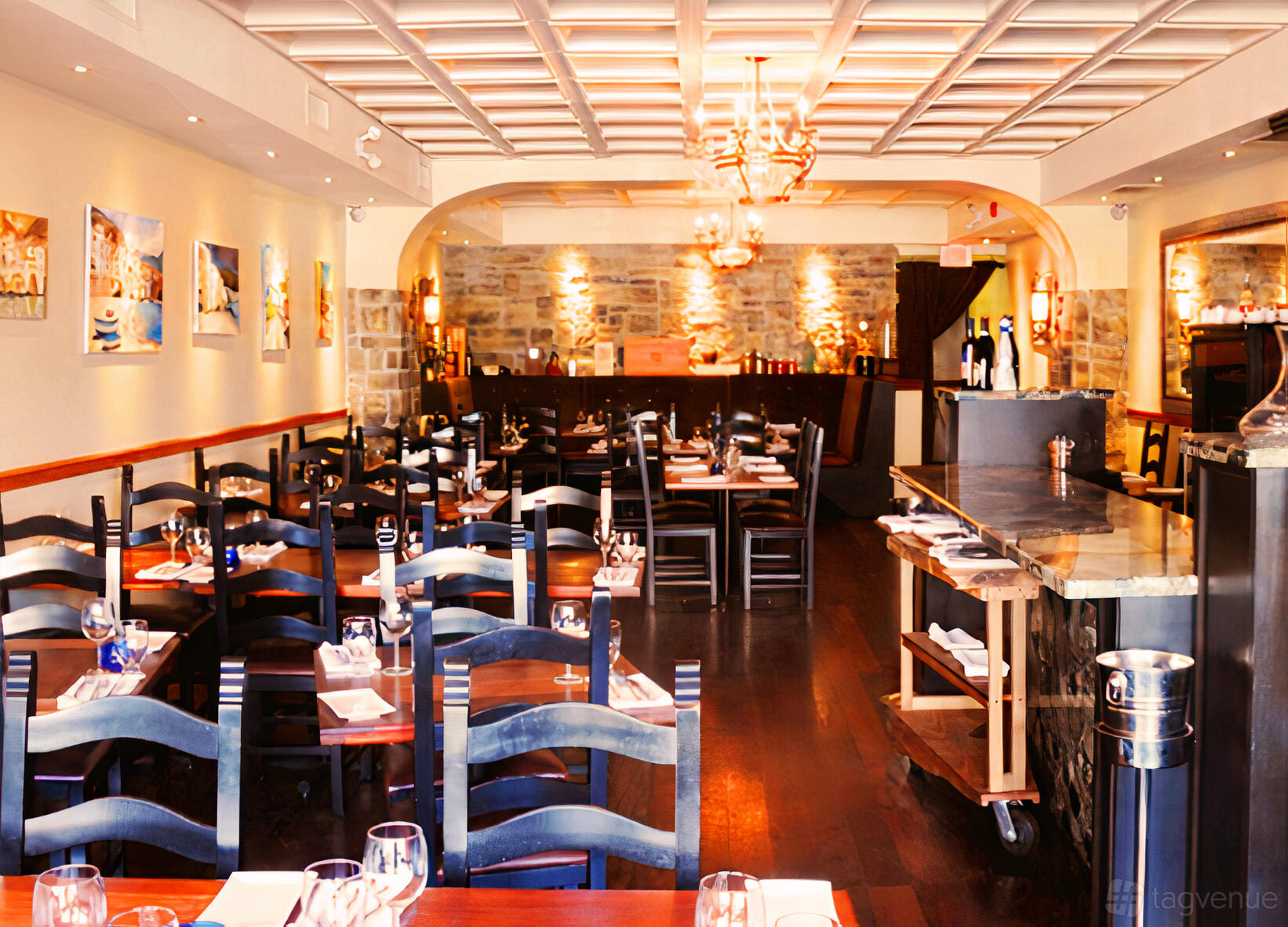 A restaurant dining area with dark wood chairs, white table settings, stone accent wall, and artwork at Pulcinella.