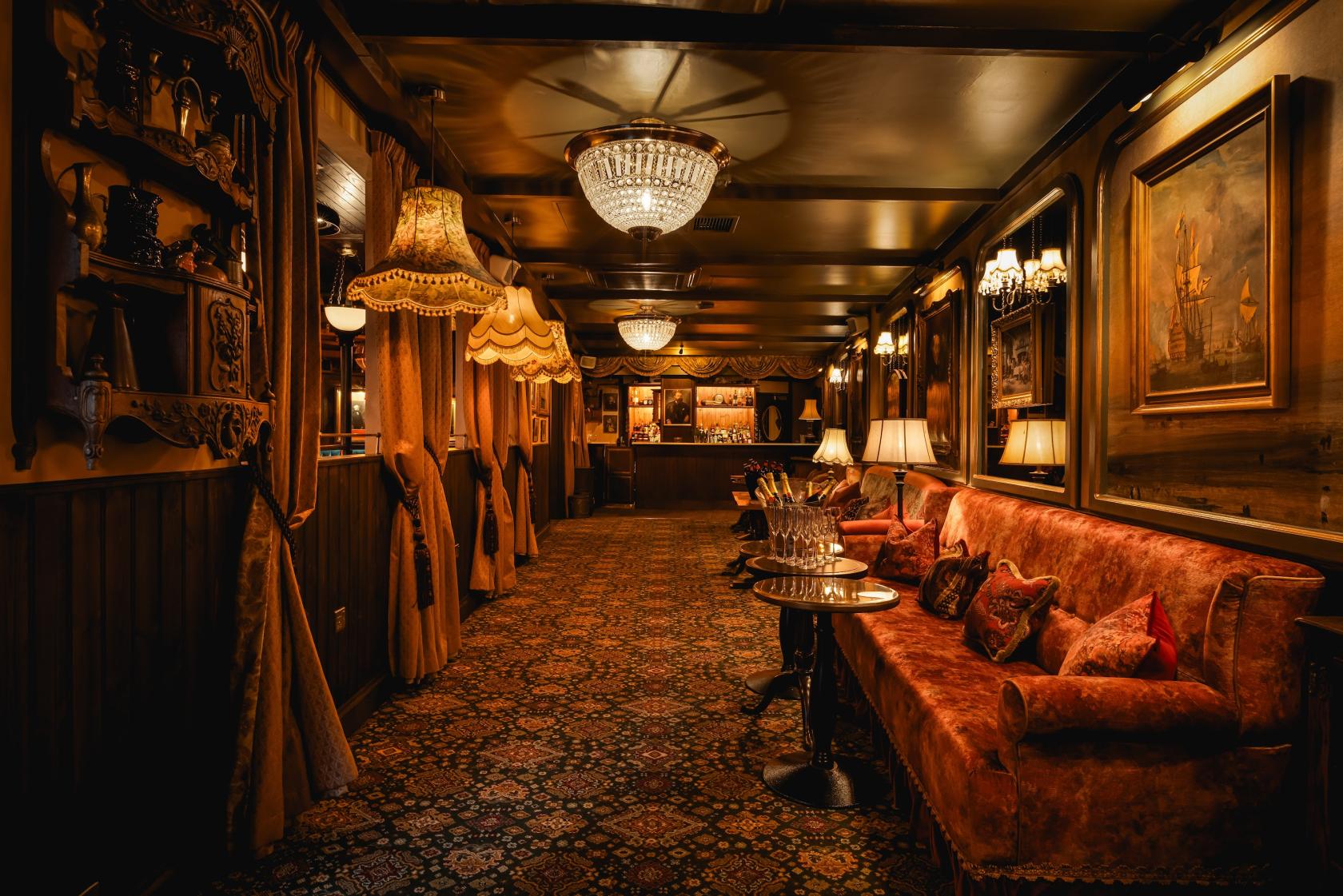 A dining room with vintage chandeliers, velvet sofas, patterned carpet, and ornate lamps at Mr Fogg's City Tavern.