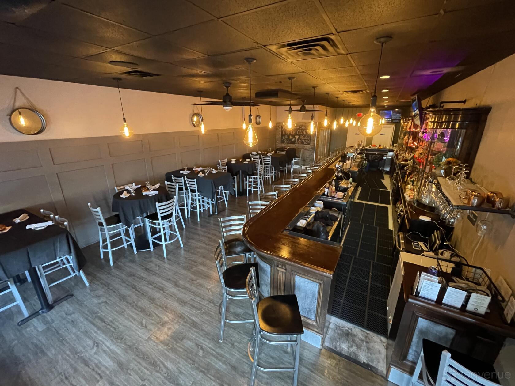 A restaurant bar area with a long wooden counter, high chairs, pendant lighting, and dining tables at Osteria 545.