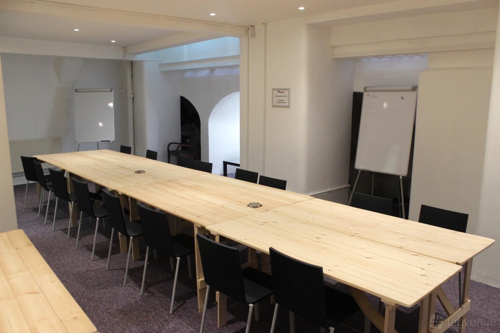 A meeting room with two long wooden tables, black chairs, and flip charts at Eastside Shoreditch.