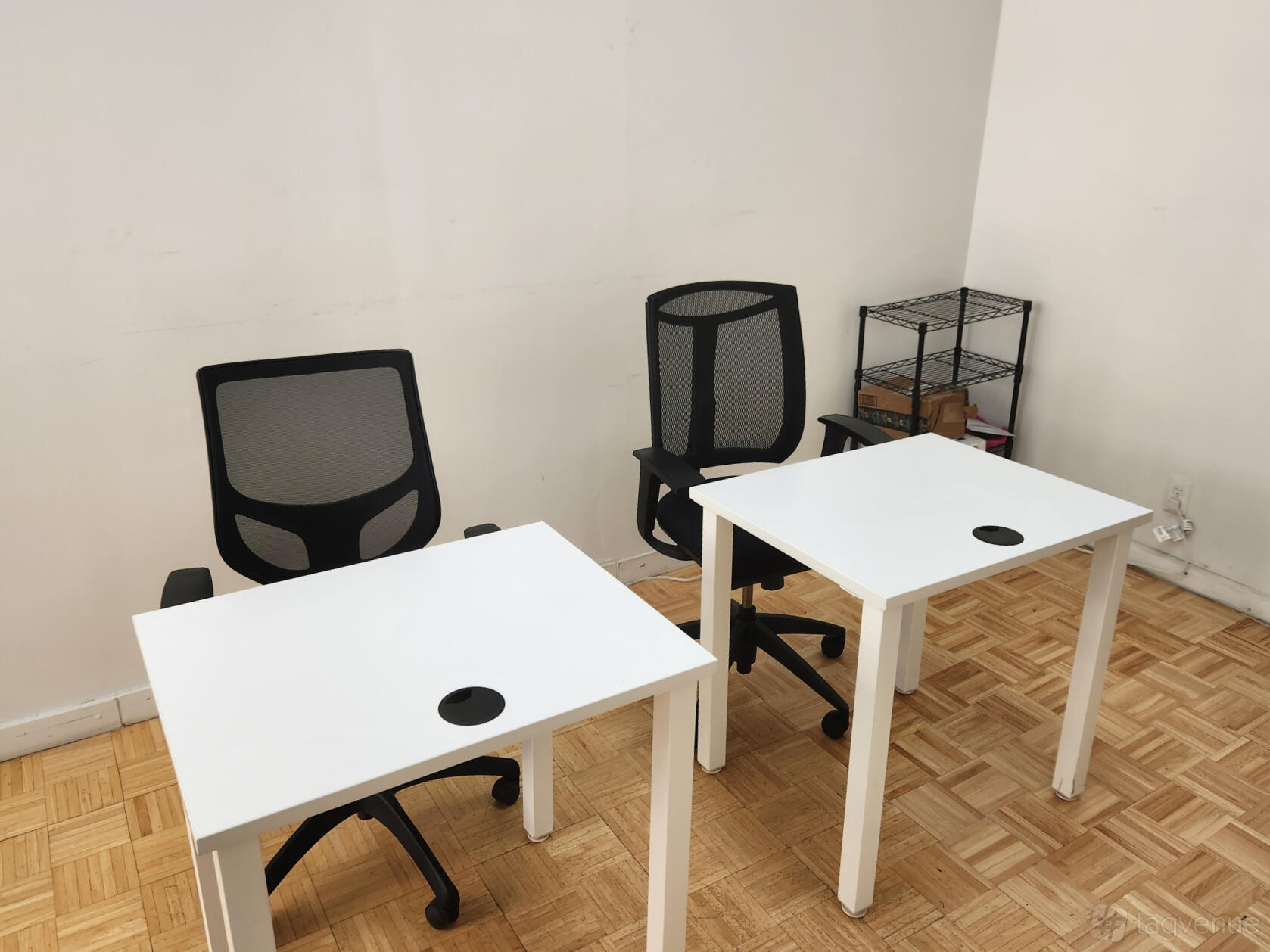 A coworking space with two mesh office chairs, white desks, and parquet flooring at SBN New York.