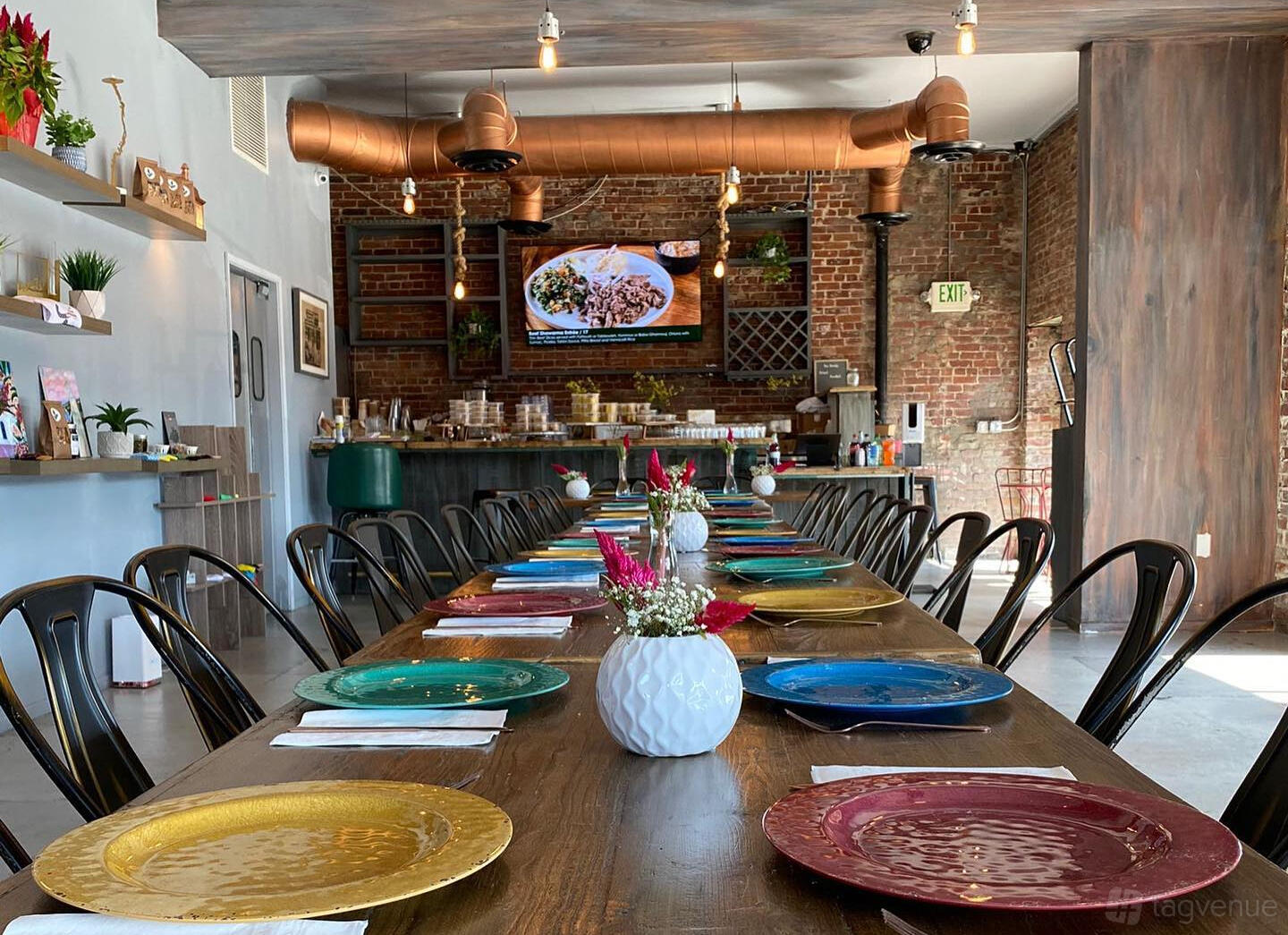 An event space in a restaurant with exposed brick walls, colorful chargers, and a long wooden table at Sumac Mediterranean Cuisine.
