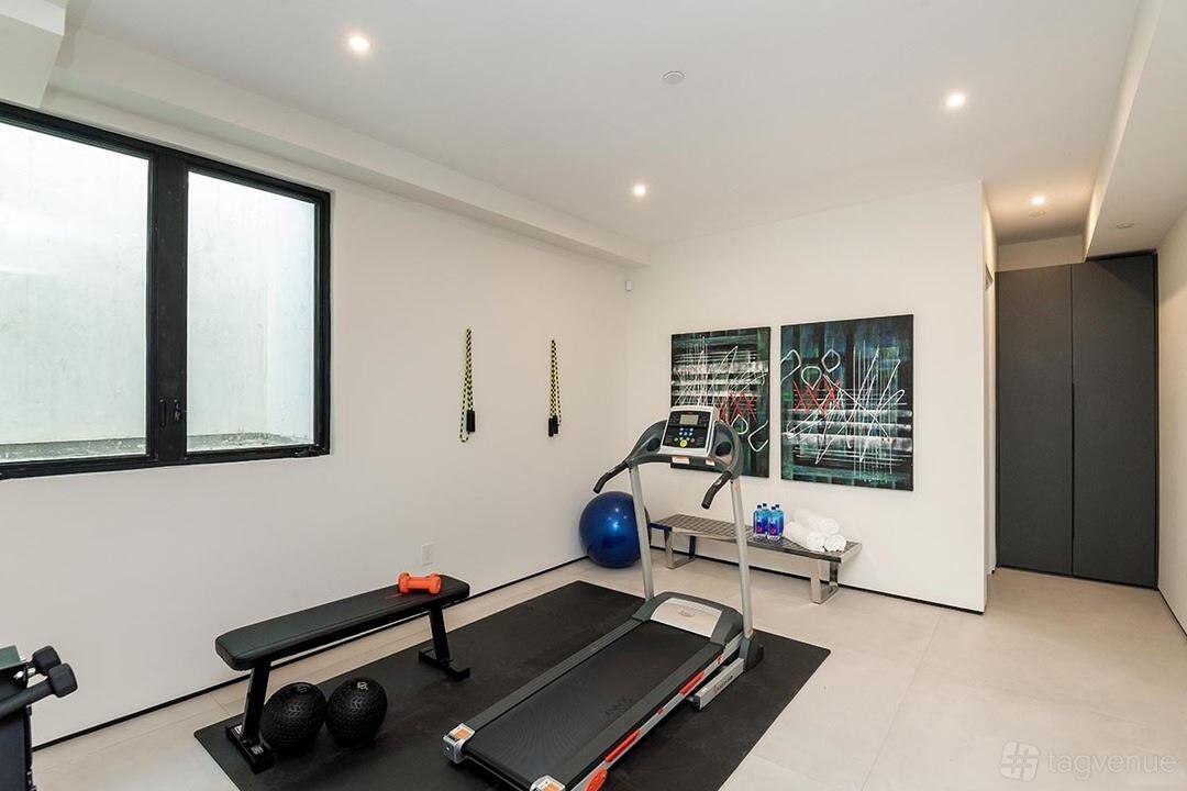 An apartment with a private gym featuring a treadmill, bench, weights, and large window at Luxury Modern Home.