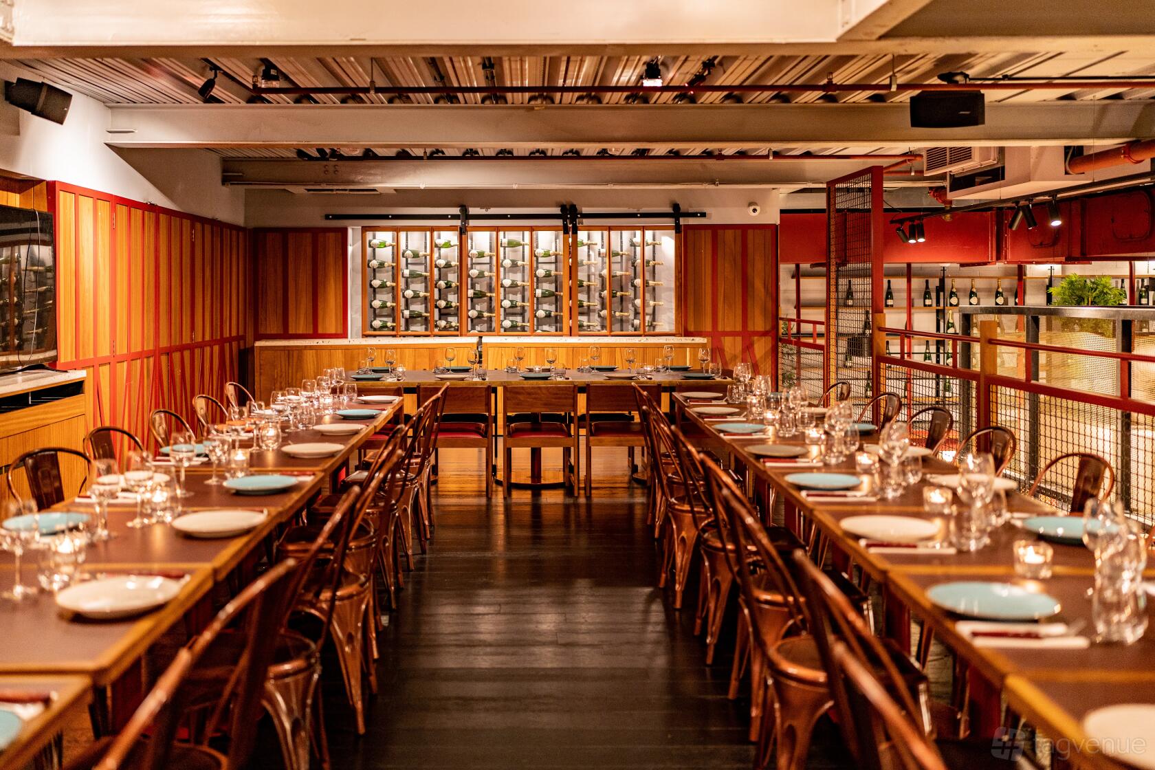 A dining room with long wooden tables, metal chairs, and a wine rack wall at temper City.