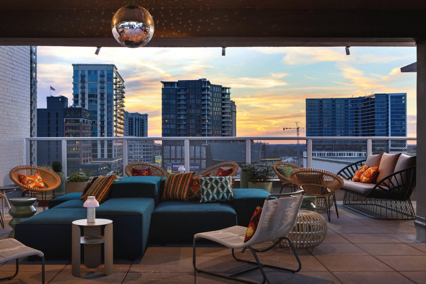 A rooftop bar with lounge seating, colorful cushions, and city skyline views at St. Julep Rooftop Bar.