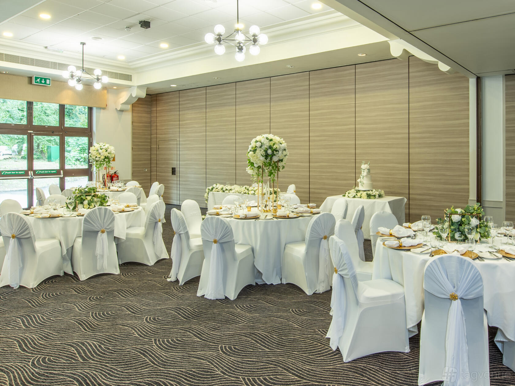 An event suite with round tables dressed in white linens, gold accents, and floral centerpieces at Mercure Brandshatch.