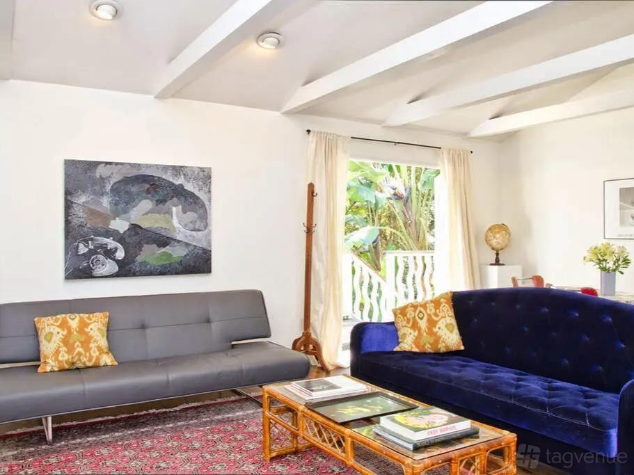 A living room with exposed ceiling beams, colorful sofas, and large windows at Hollywood Craftsman Home.