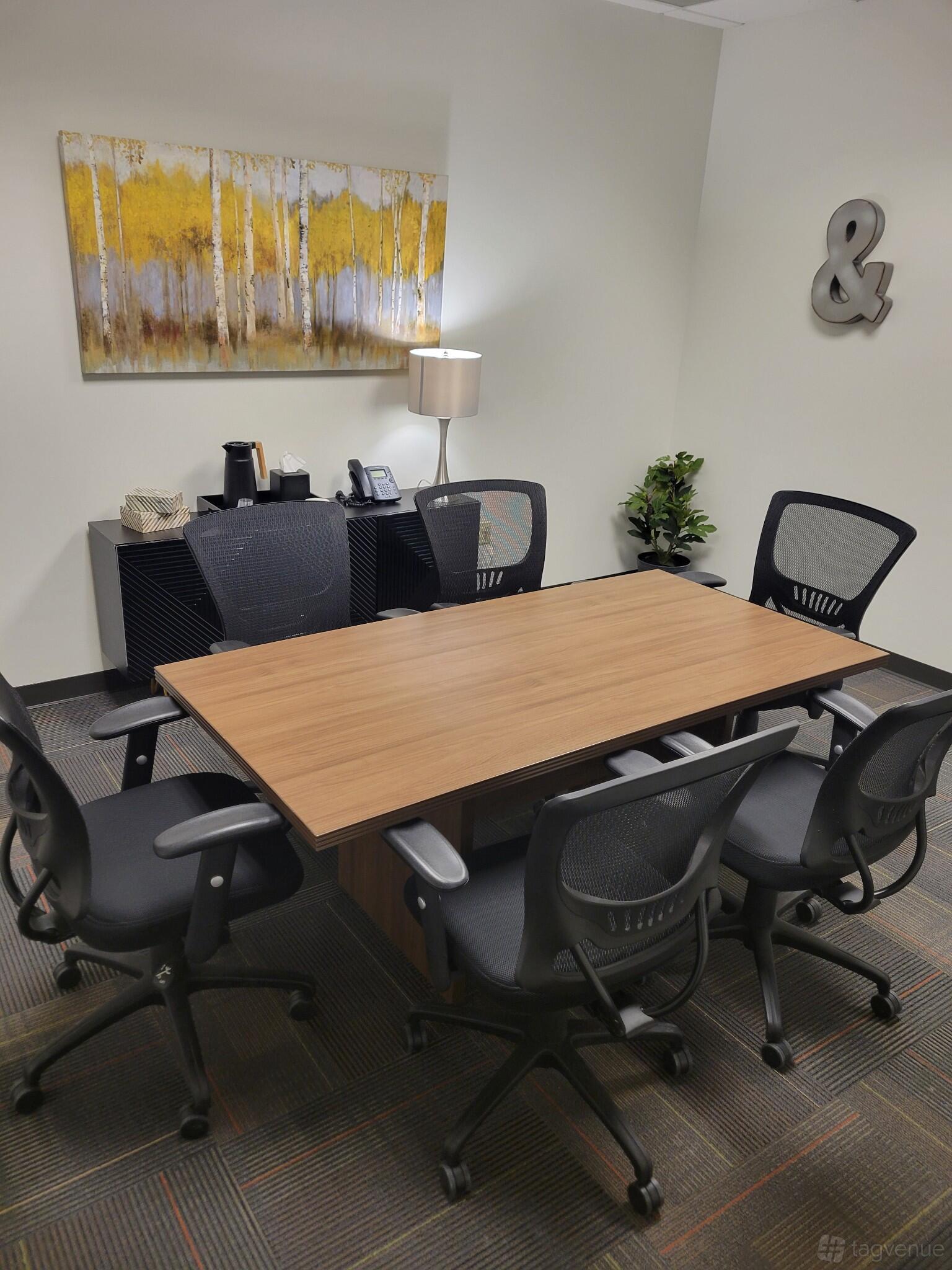 A coworking space with a wooden conference table, six mesh chairs, and a sideboard with coffee service at Executive Workspace Allen Center.