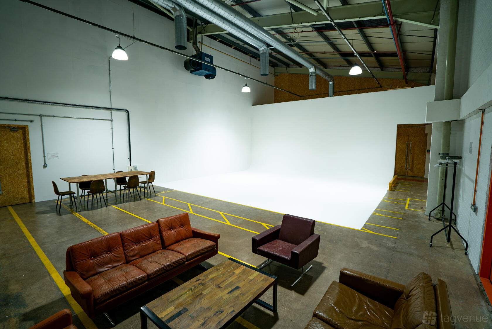 A photo studio with a white cyclorama wall, exposed ductwork, and leather seating at Un.titled Studio.