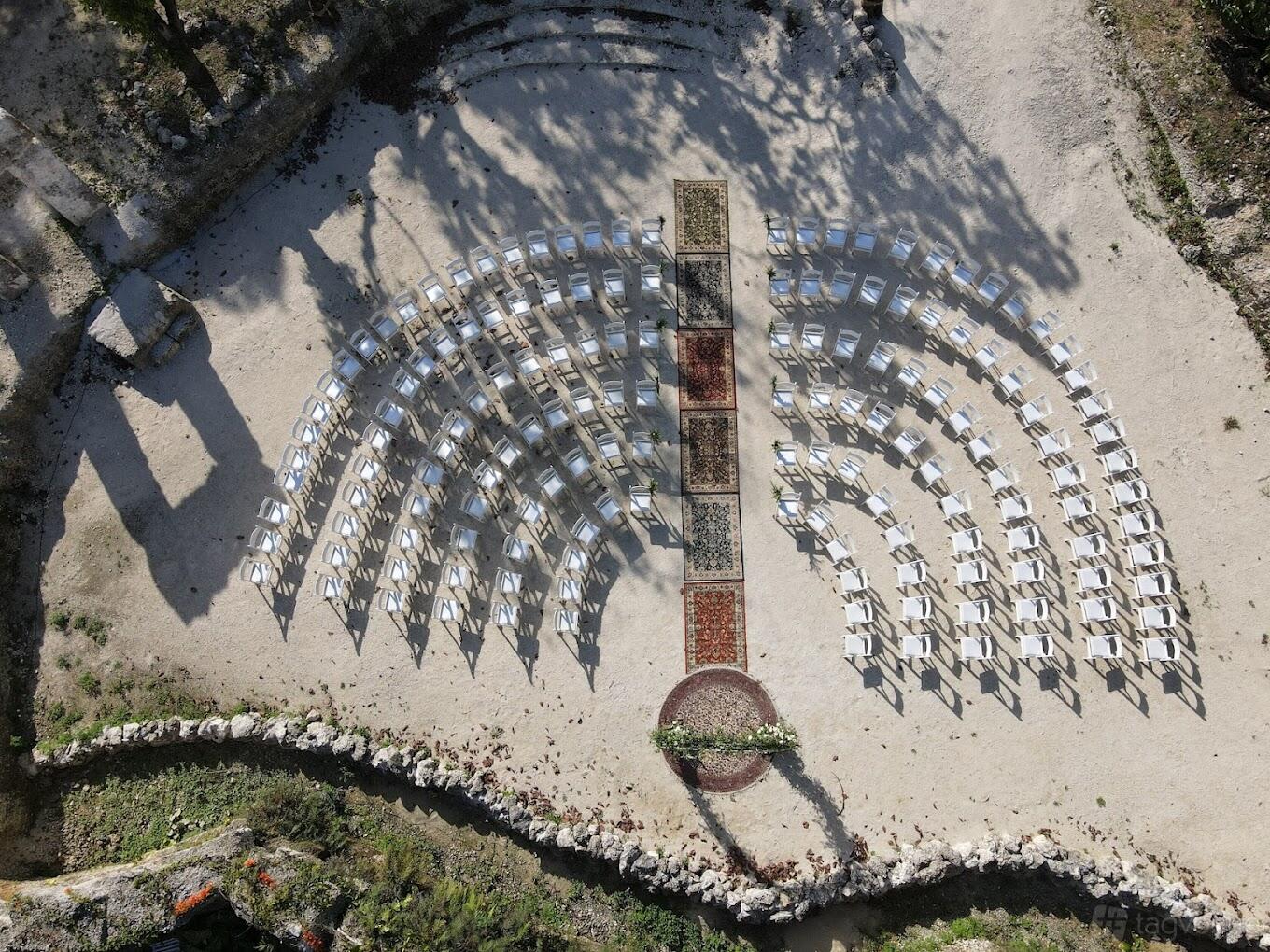 An outdoor restaurant space with rows of white chairs arranged in an arc and a central aisle at Mon Petit.