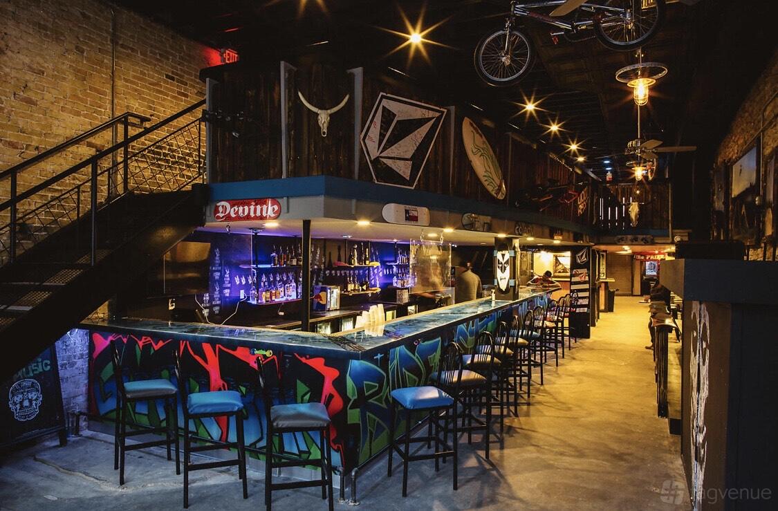 An event space in a bar with a graffiti-covered bar counter, high stools, exposed brick walls, and overhead bike decor at Gnar Bar.