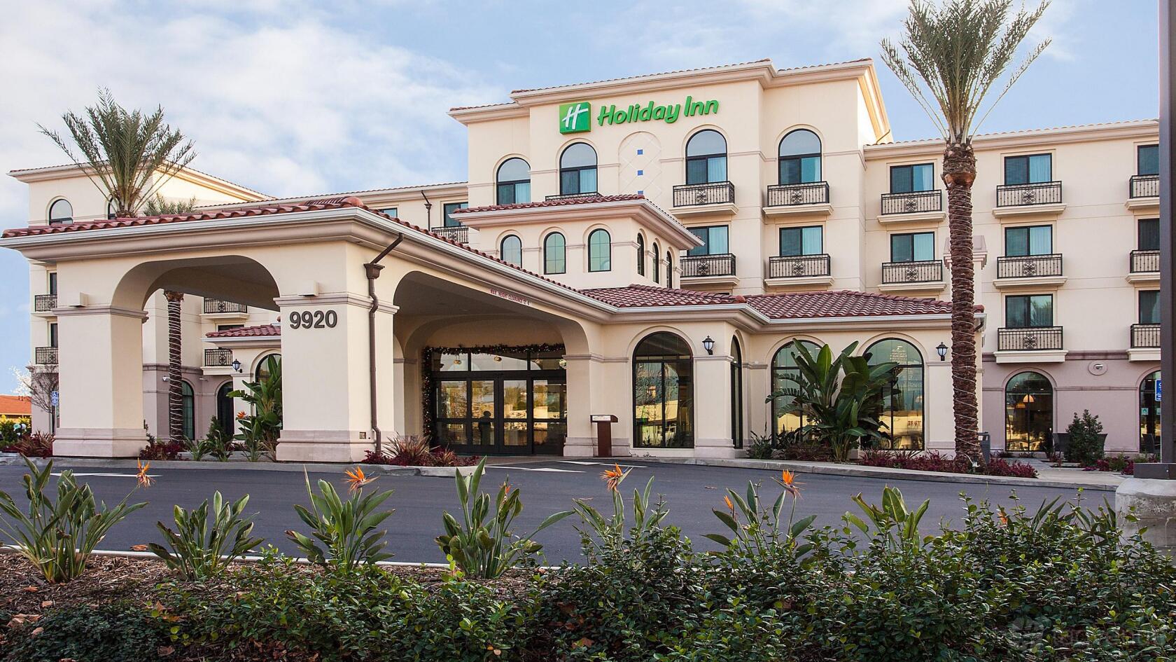 A hotel entrance with an arched driveway, palm trees, and stucco exterior at Holiday Inn El Monte.