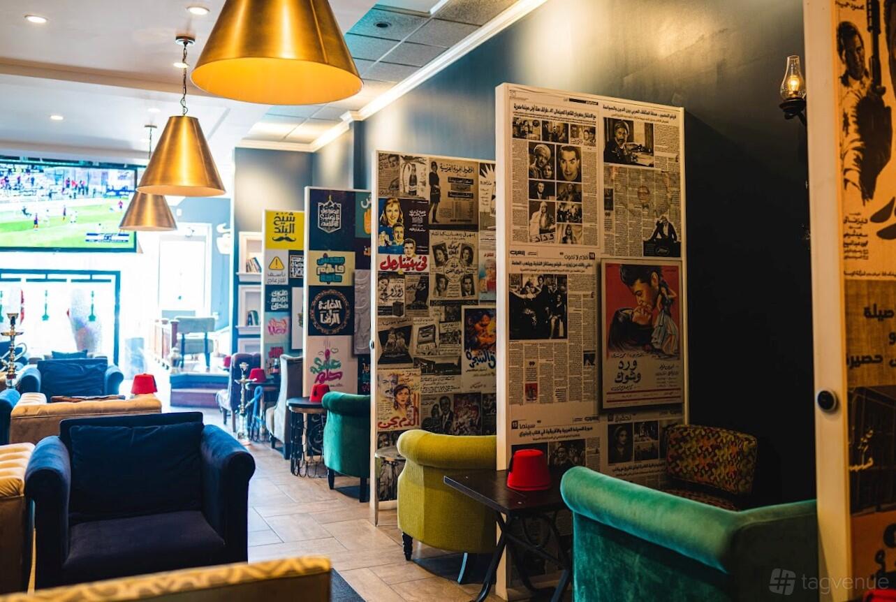 A bar with colorful velvet armchairs, newspaper-covered walls, and pendant lighting at AFANDINA HOOKAH LOUNGE.