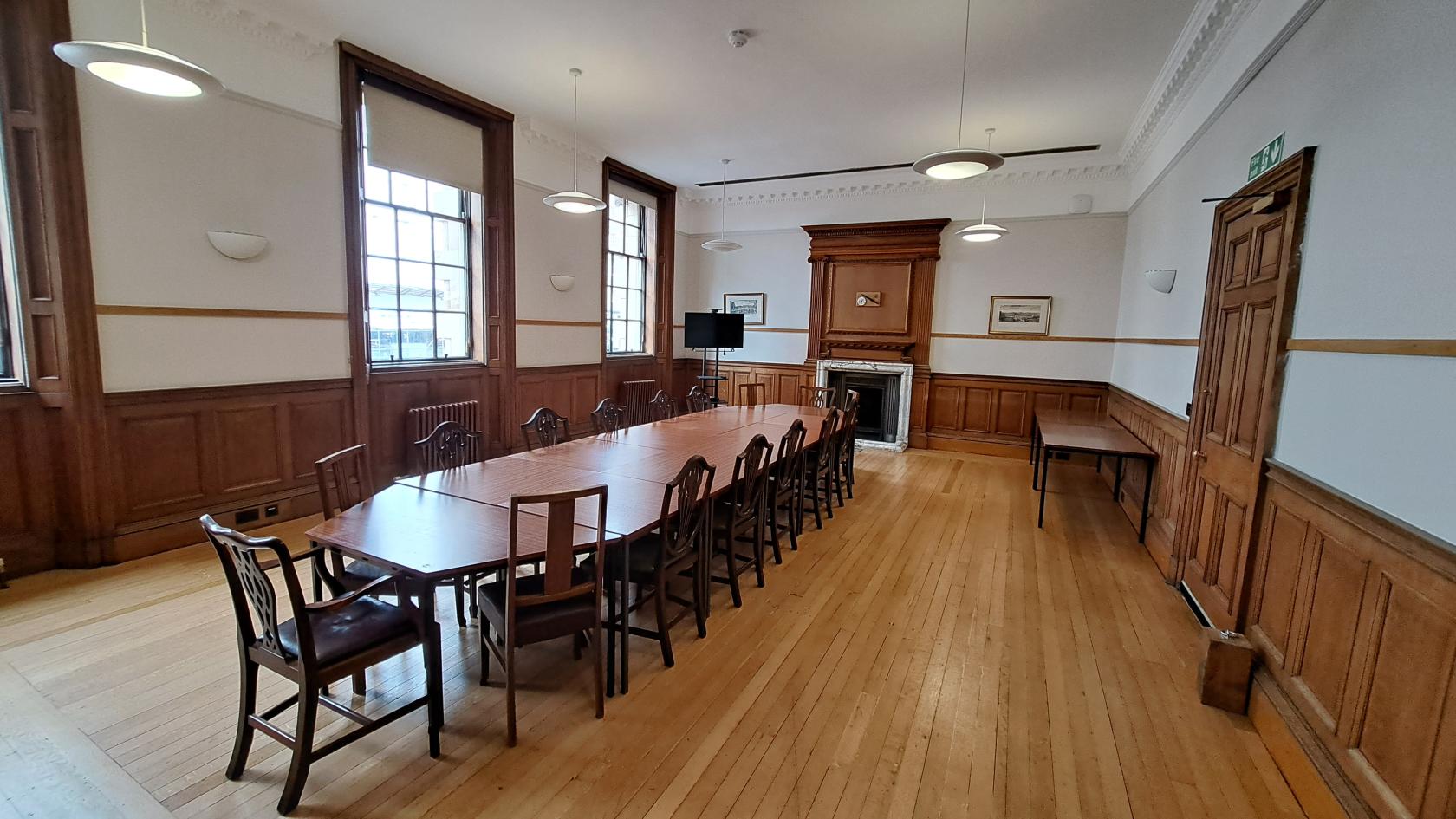 An event venue with tall windows, wood paneling, a long meeting table, and a decorative fireplace at Institut francais d'Ecosse.
