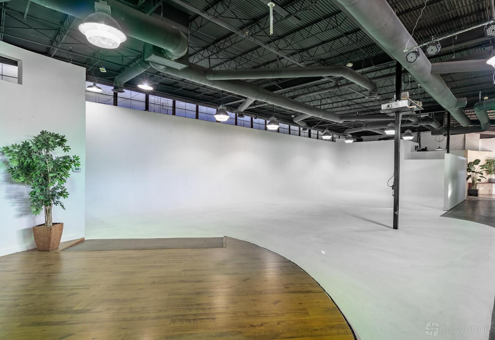 An event venue with white curved walls, high ceilings, exposed ductwork, and wood flooring at Royal Lane Studios.
