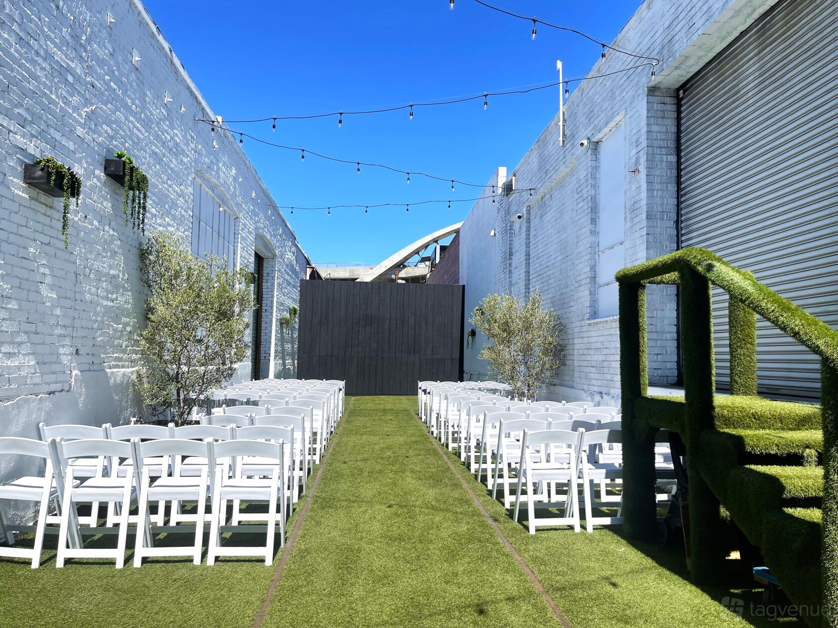An outdoor event space with artificial turf, white folding chairs, and string lights at The East Angel.