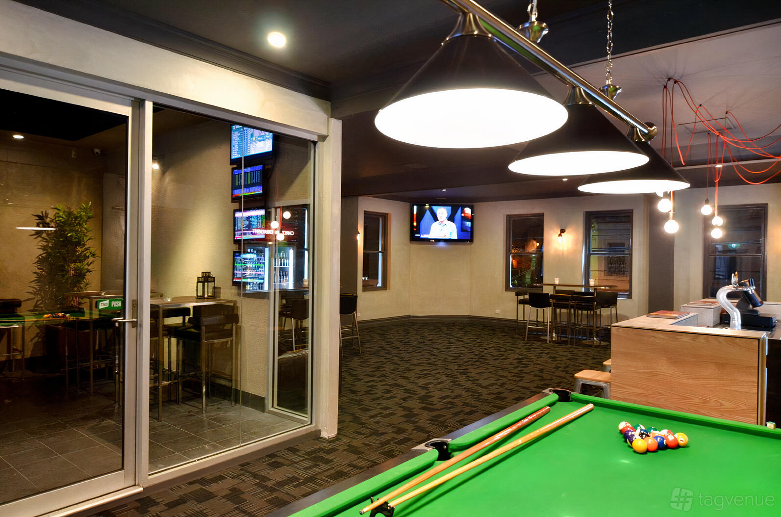An event space in a pub with a pool table, overhead pendant lights, and wall-mounted TVs at Bakers Arms.