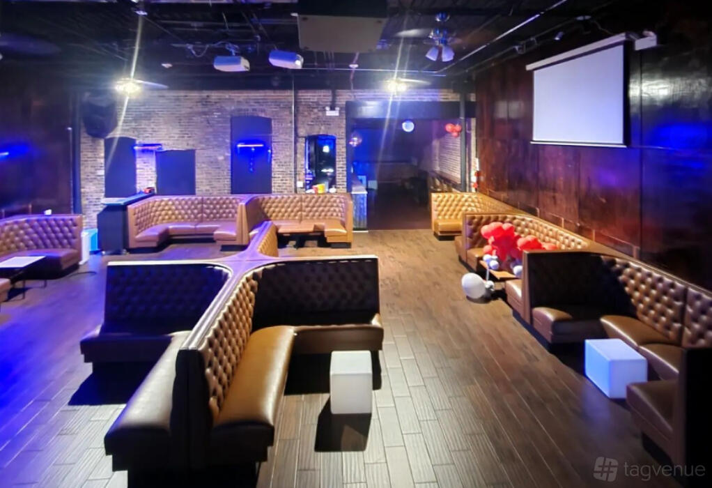 An event space in a bar with tufted brown leather booths, wood flooring, and exposed brick walls at Mikes Place Sports Bar & Grill.