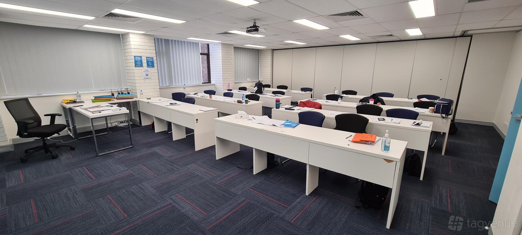 A training room with rows of white desks, blue chairs, and a projector at Vigil Training College.