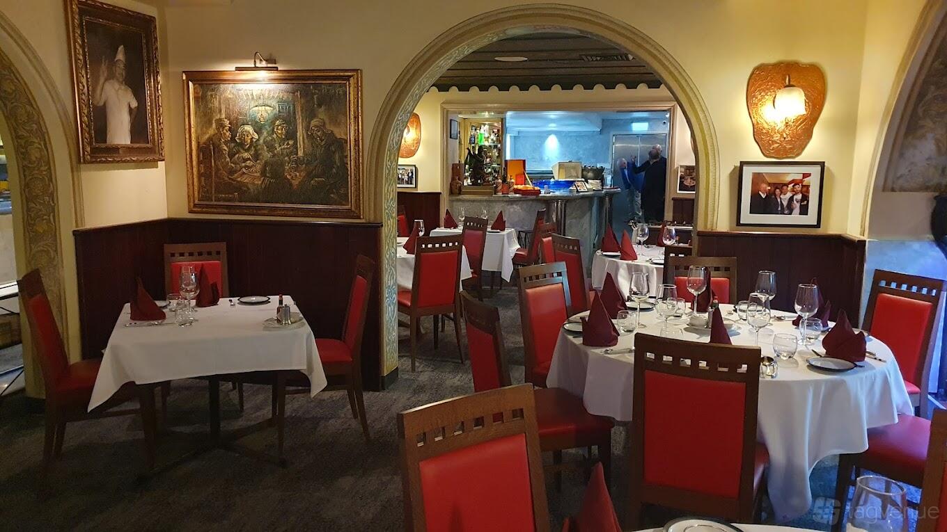 A restaurant with red cushioned chairs, white tablecloths, and classic paintings on the walls at Blue Angel.