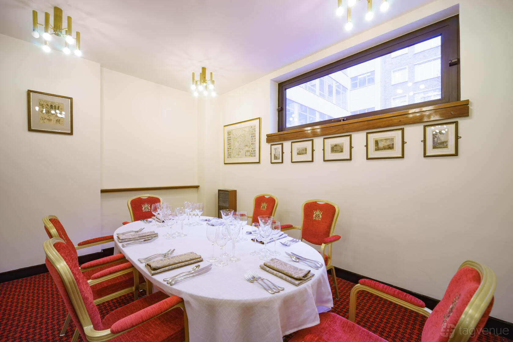 A meeting room with red upholstered chairs, framed wall art, and a window with city views at Bakers' Hall.