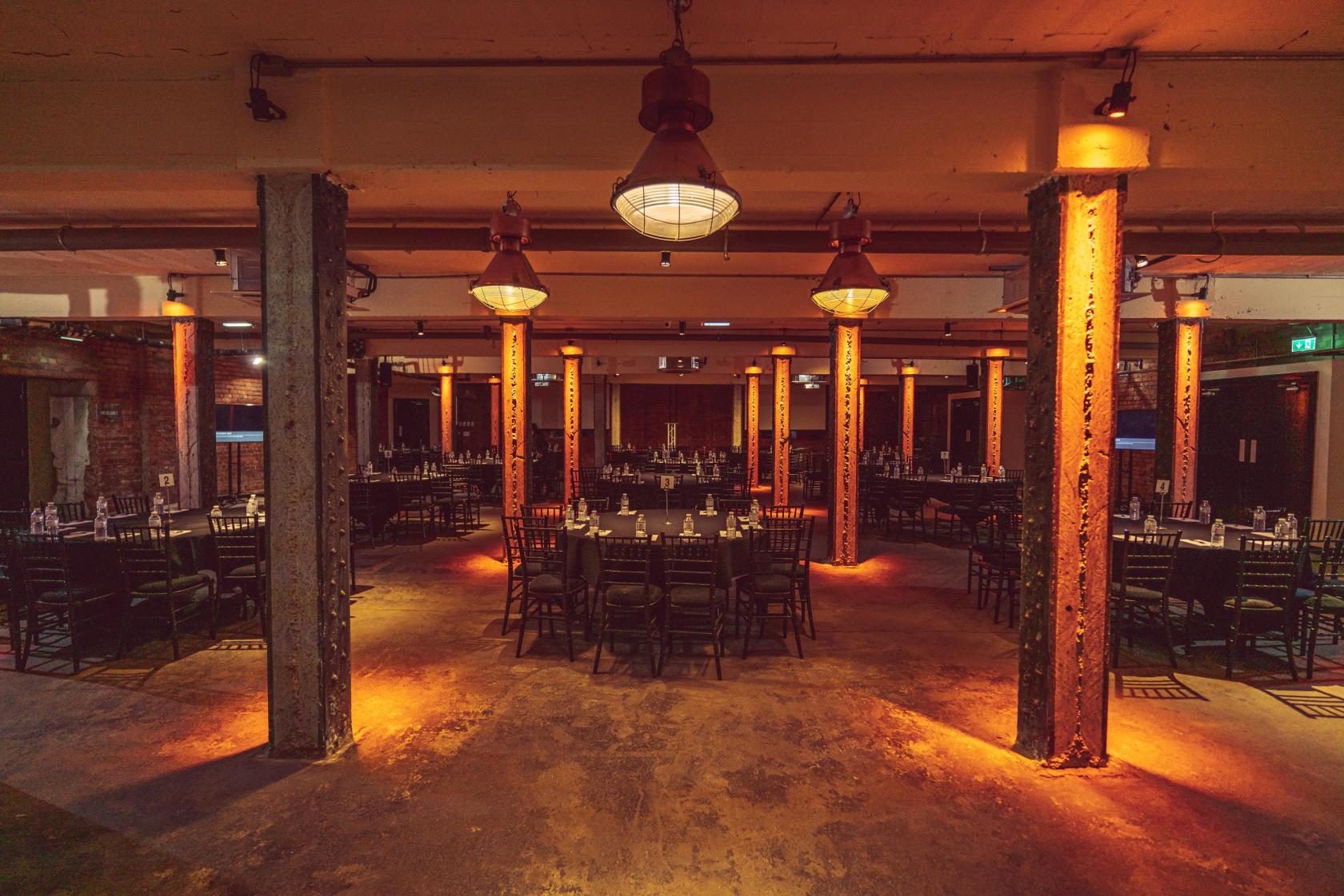 An event space in a warehouse with exposed beams, industrial pillars, and rows of banquet tables at Victoria Warehouse.