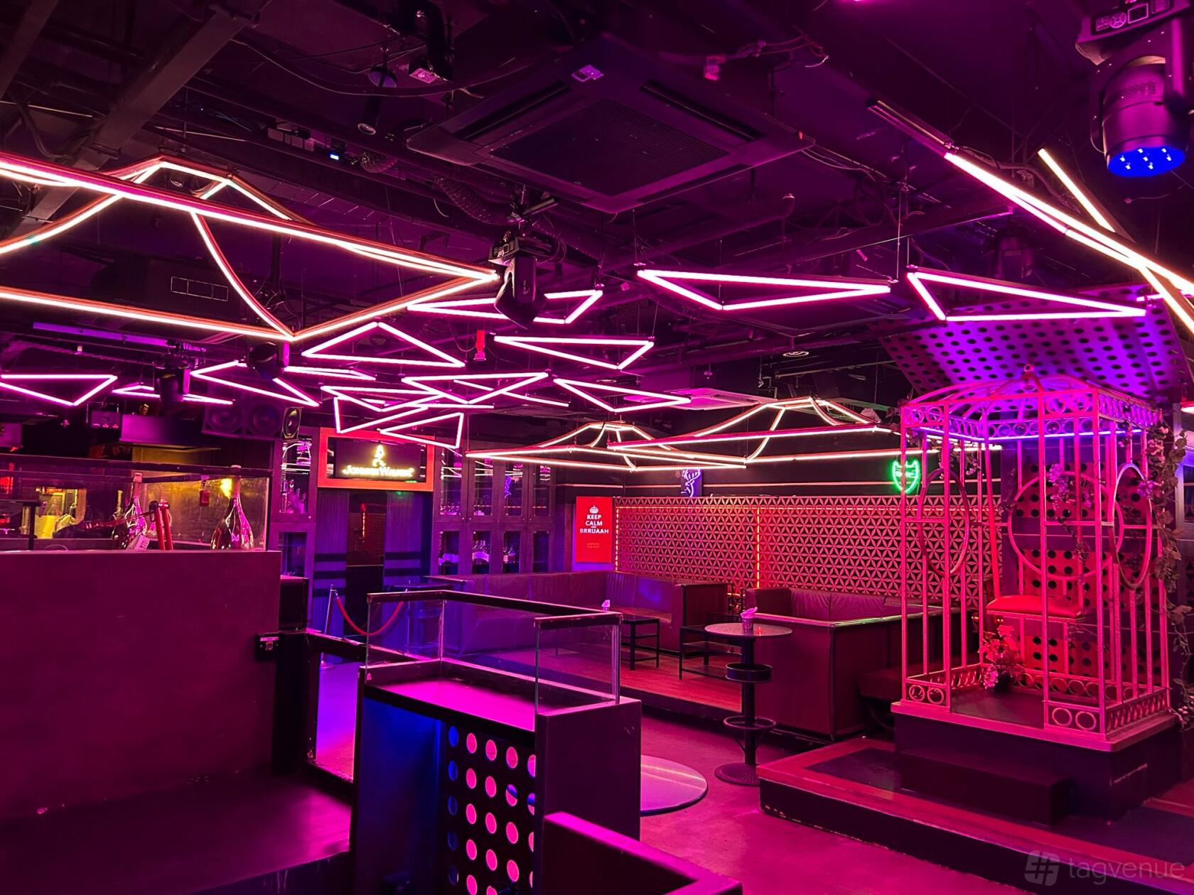 A nightclub with geometric neon ceiling lights, lounge seating, and a decorative cage at Magic Carpet Lounge.
