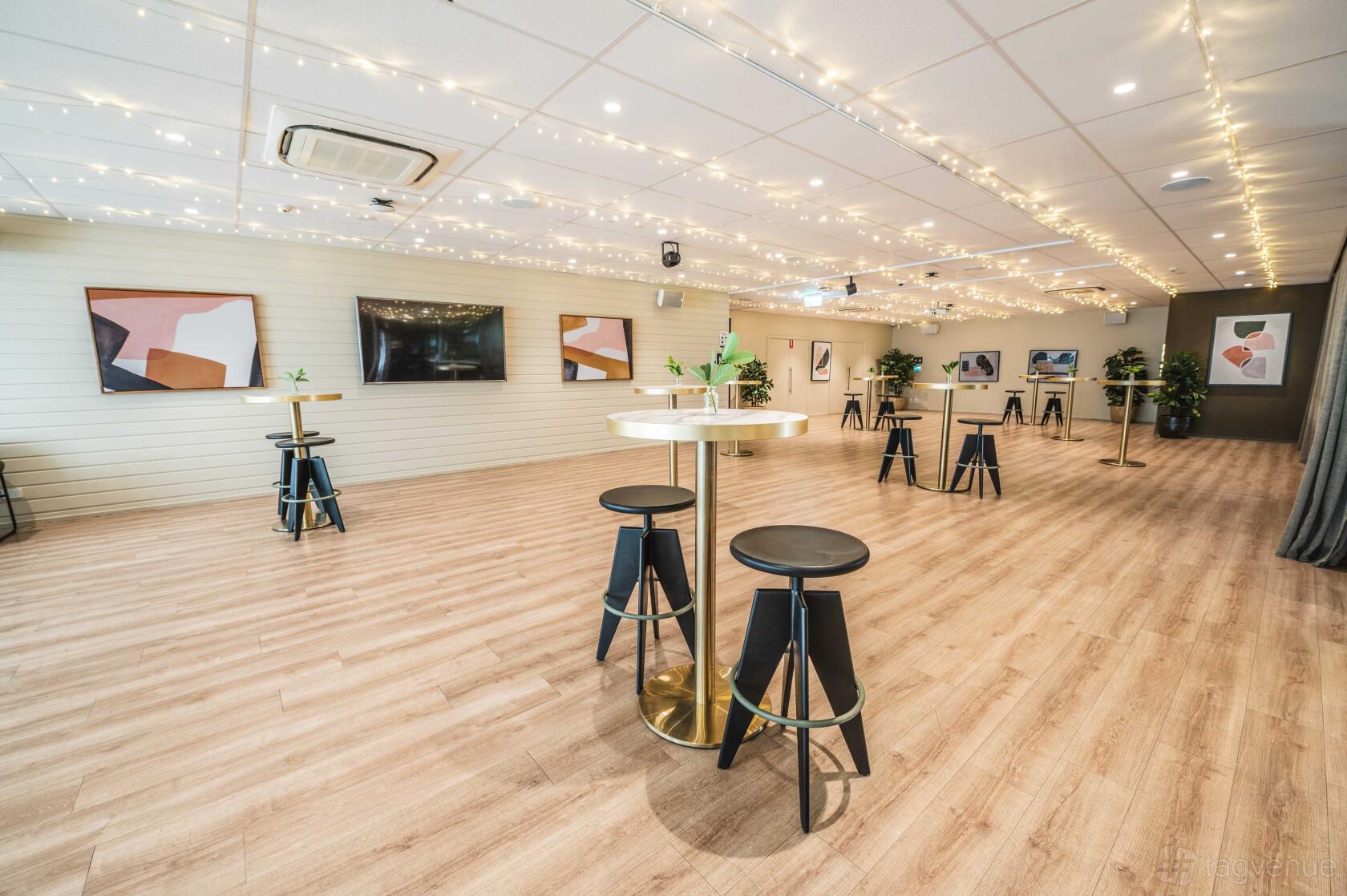 An event room with wood floors, string lights across the ceiling, and cocktail tables with stools at The Alcott.