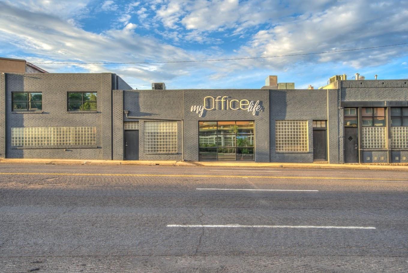 A coworking space with a gray brick exterior, glass block windows, and large signage at myOfficeLife.