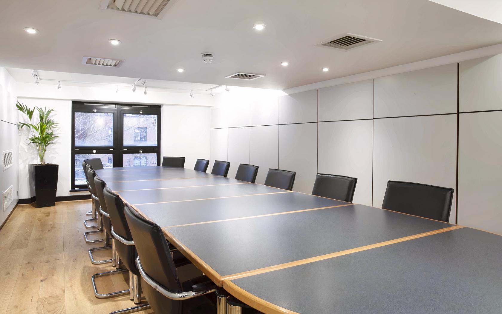 A boardroom with a long table, black chairs, wood flooring, and large windows at Whitefriars Bristol.