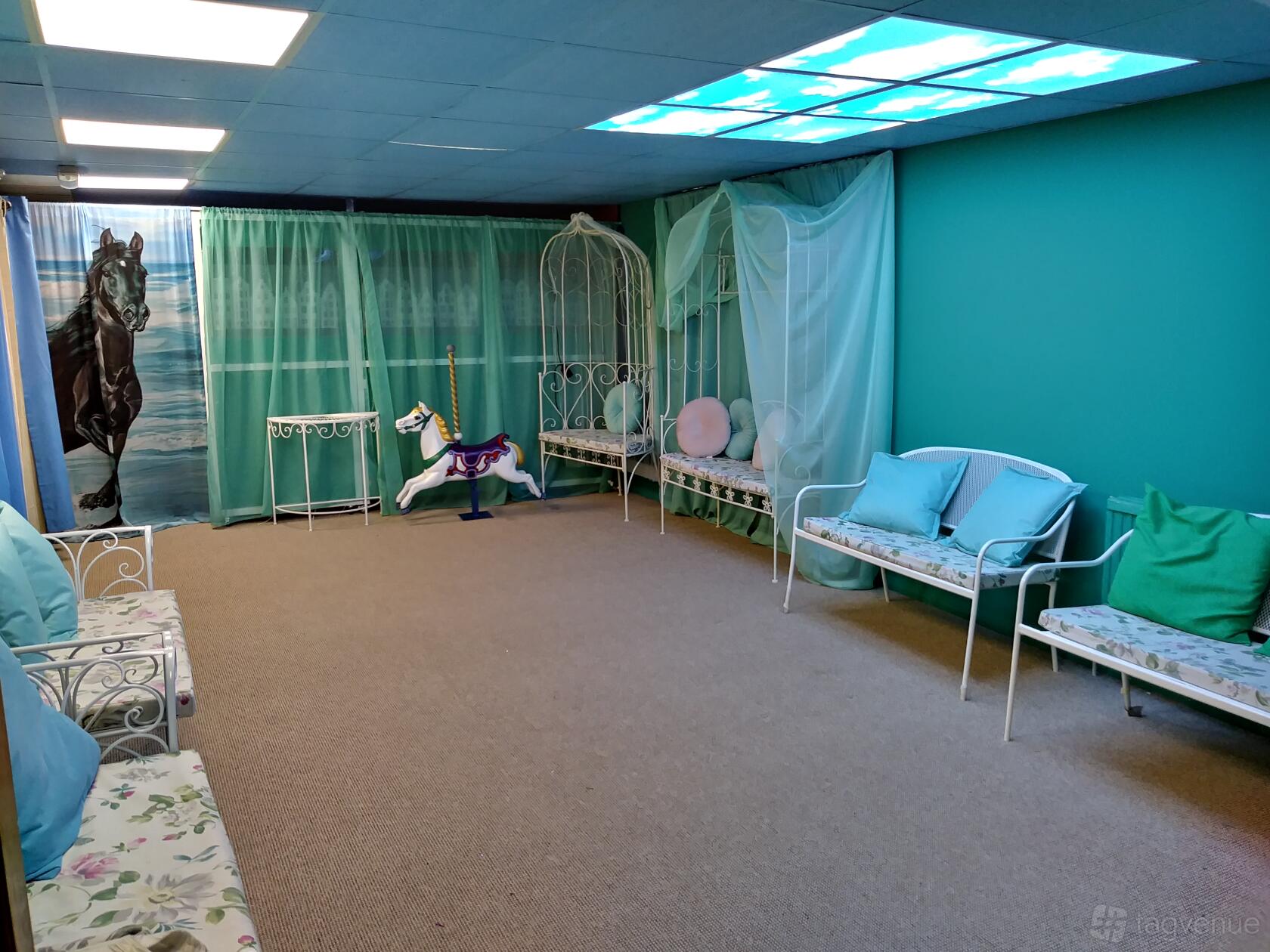 An event venue with pastel walls, cushioned benches, a carousel horse, and decorative drapery at Vintage Playroom