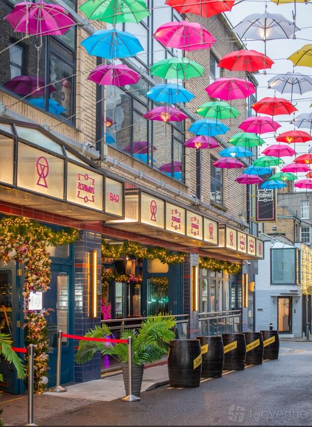 A cocktail bar with colorful umbrellas suspended above the entrance and illuminated marquee signs at Zozimus Bar.