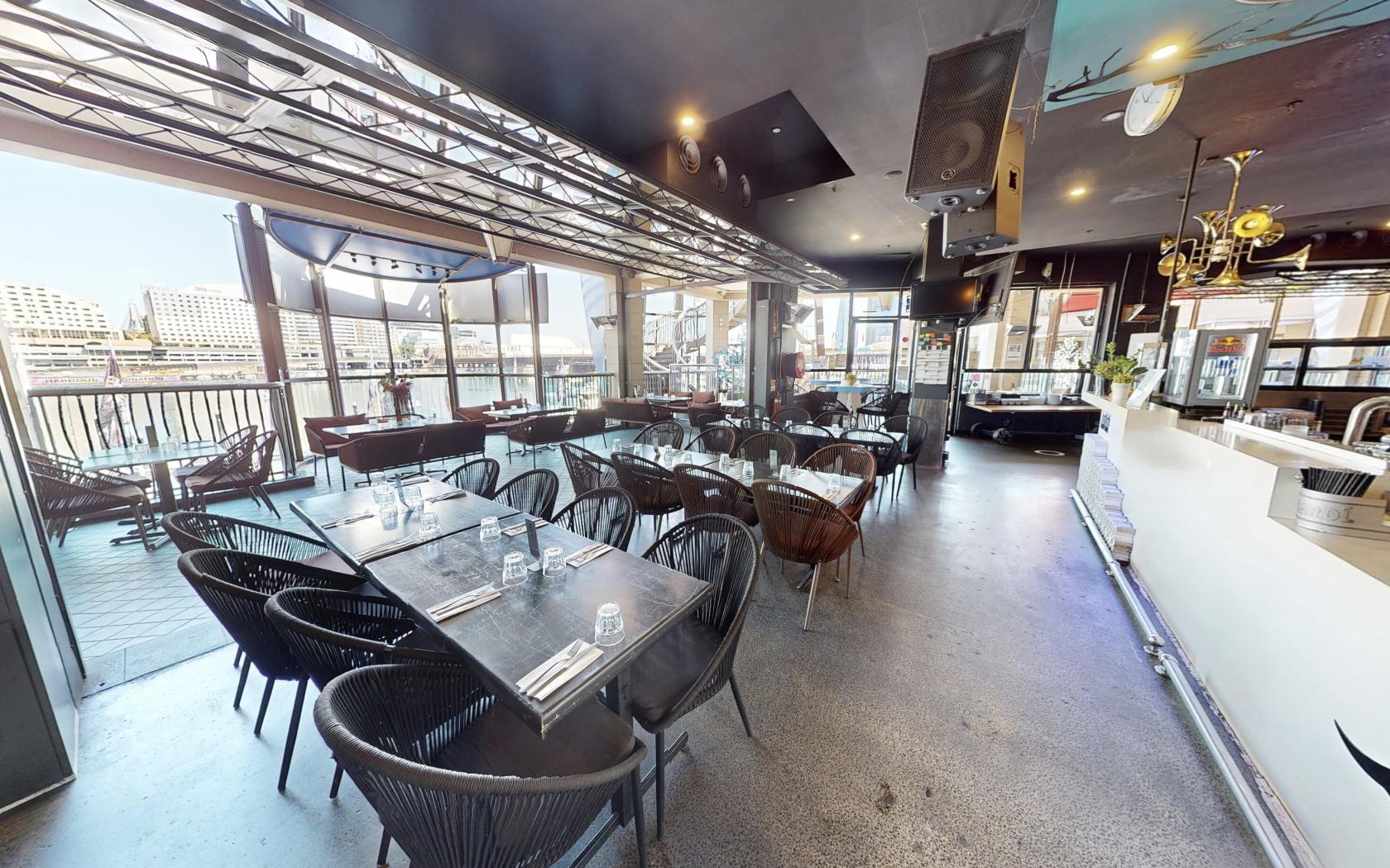 An outdoor dining area with black woven chairs, glass-topped tables, and water views at Blackbird Cafe.
