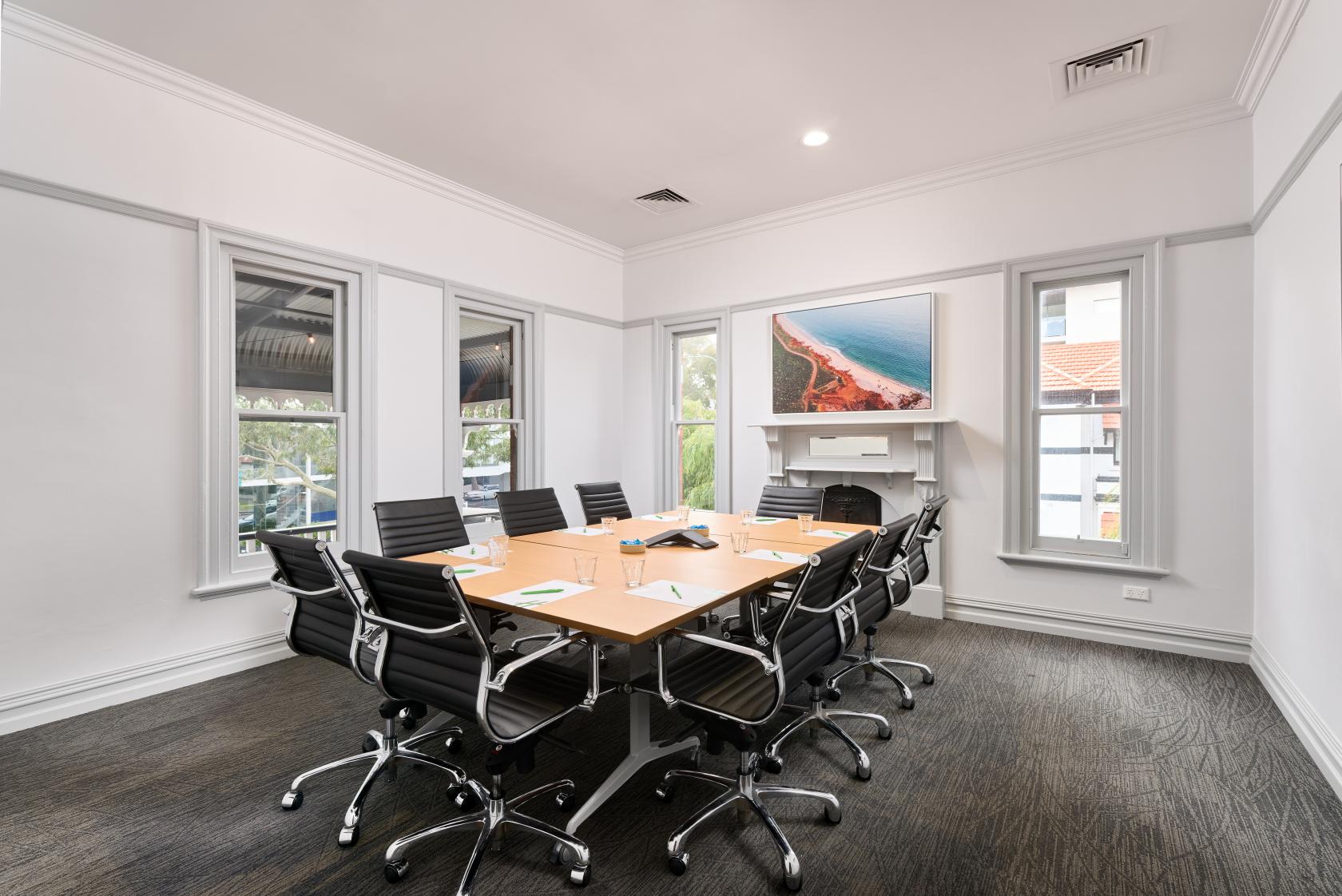 A hotel meeting room with a rectangular wooden table, black swivel chairs, and large windows at Holiday Inn West Perth.