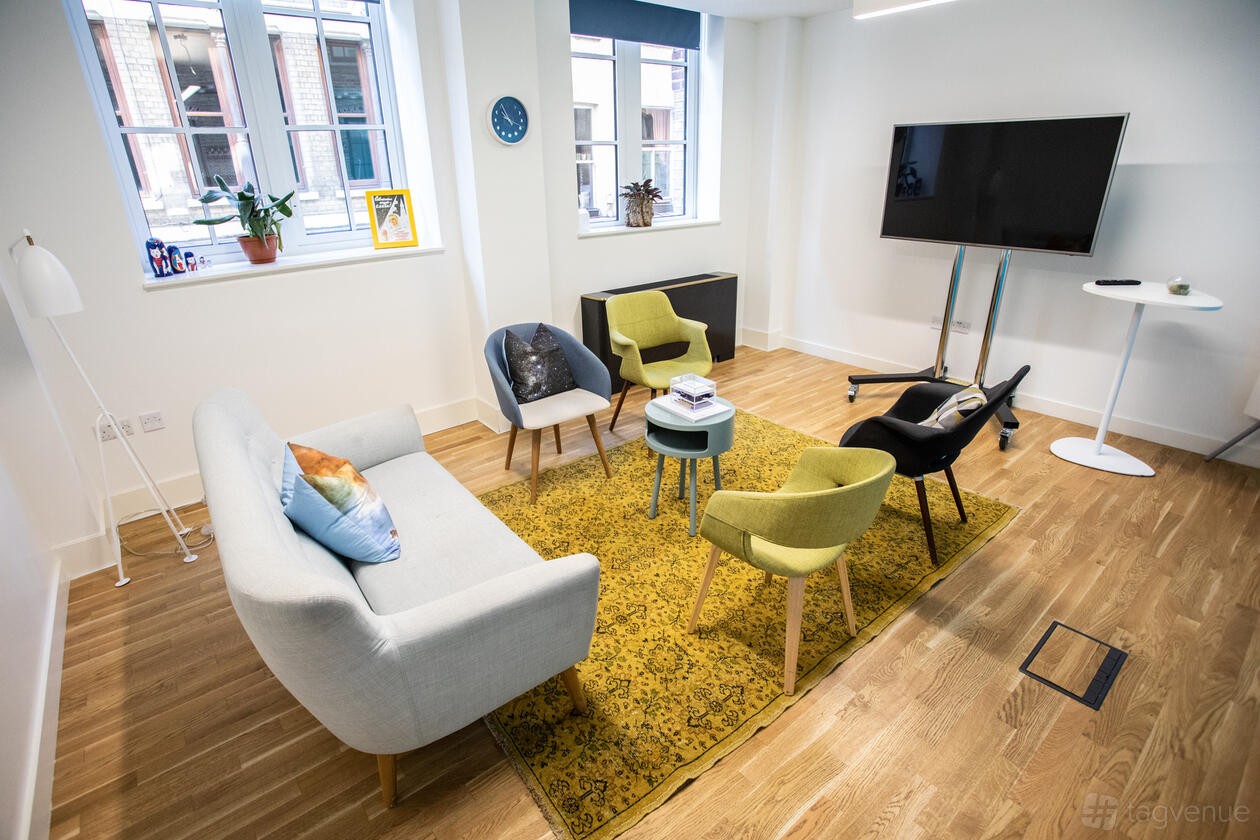 A meeting room with a sofa, colorful chairs, a yellow rug, and a large TV screen at Wallacespace Spitalfields.