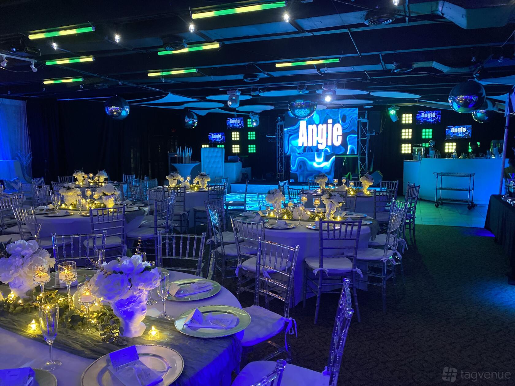 An event venue with round tables set with white linens, glowing centerpieces, and a lit dance floor at Ritmos West.