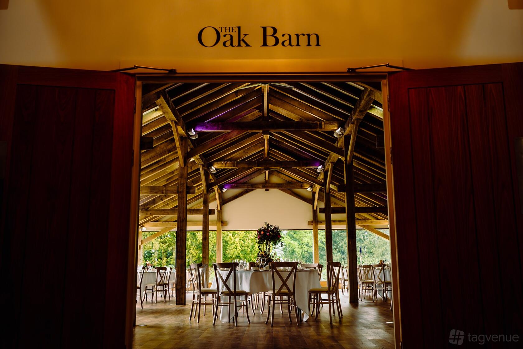 A barn venue with exposed wooden beams, round tables, and large windows at Bredenbury Court Barns.