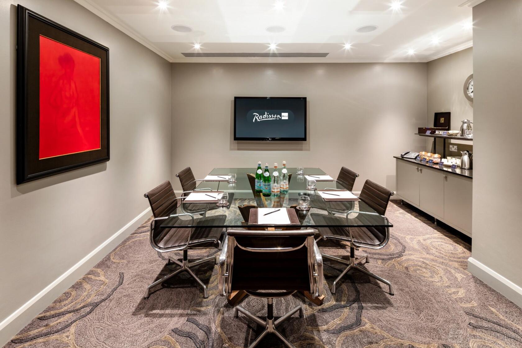 A meeting room with a glass conference table, leather chairs, wall-mounted screen, and refreshments at Radisson Blu Hotel, London Euston Square.