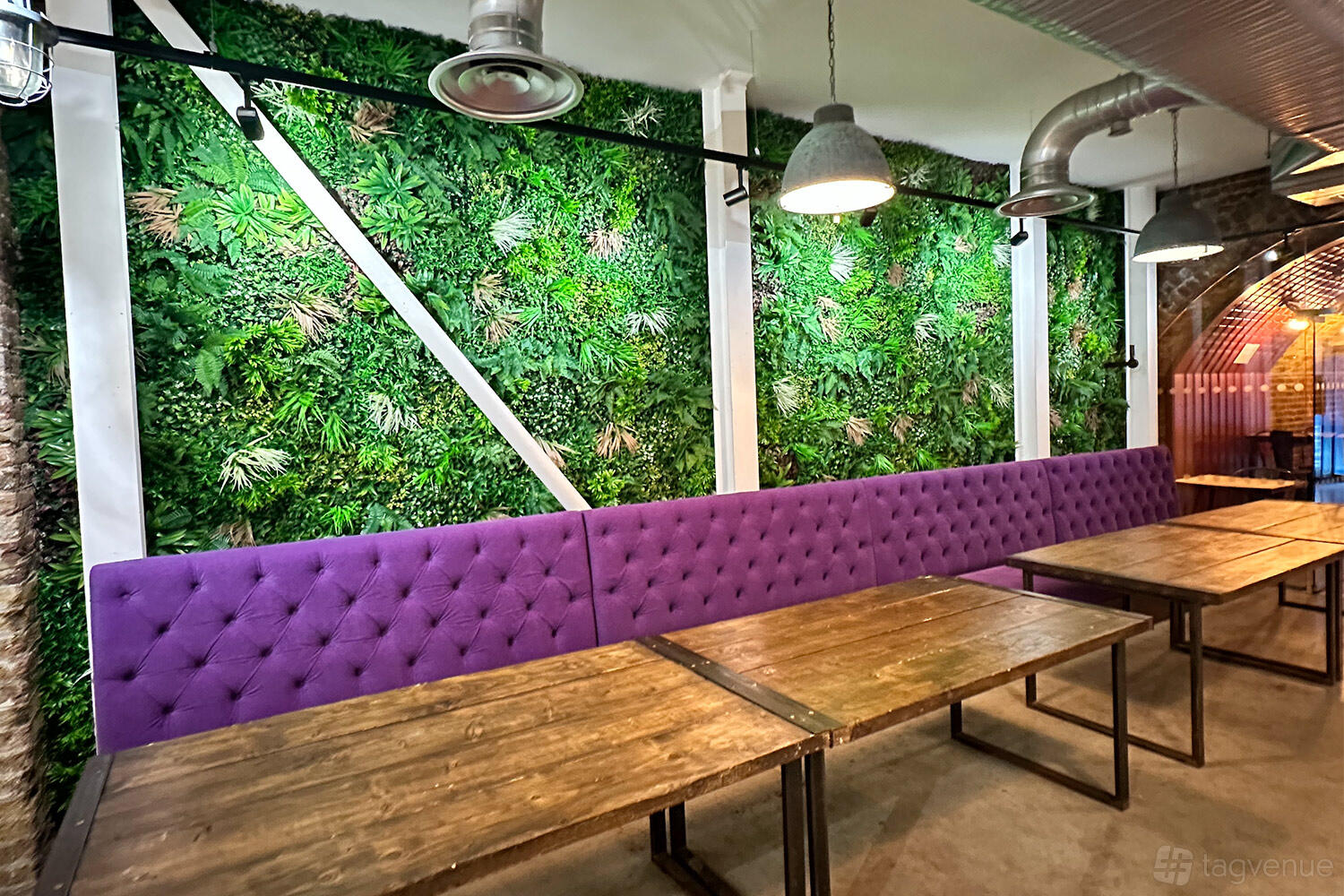 An event space in a bar with a green plant wall, purple bench seating, and wooden tables at SAMA Bankside.