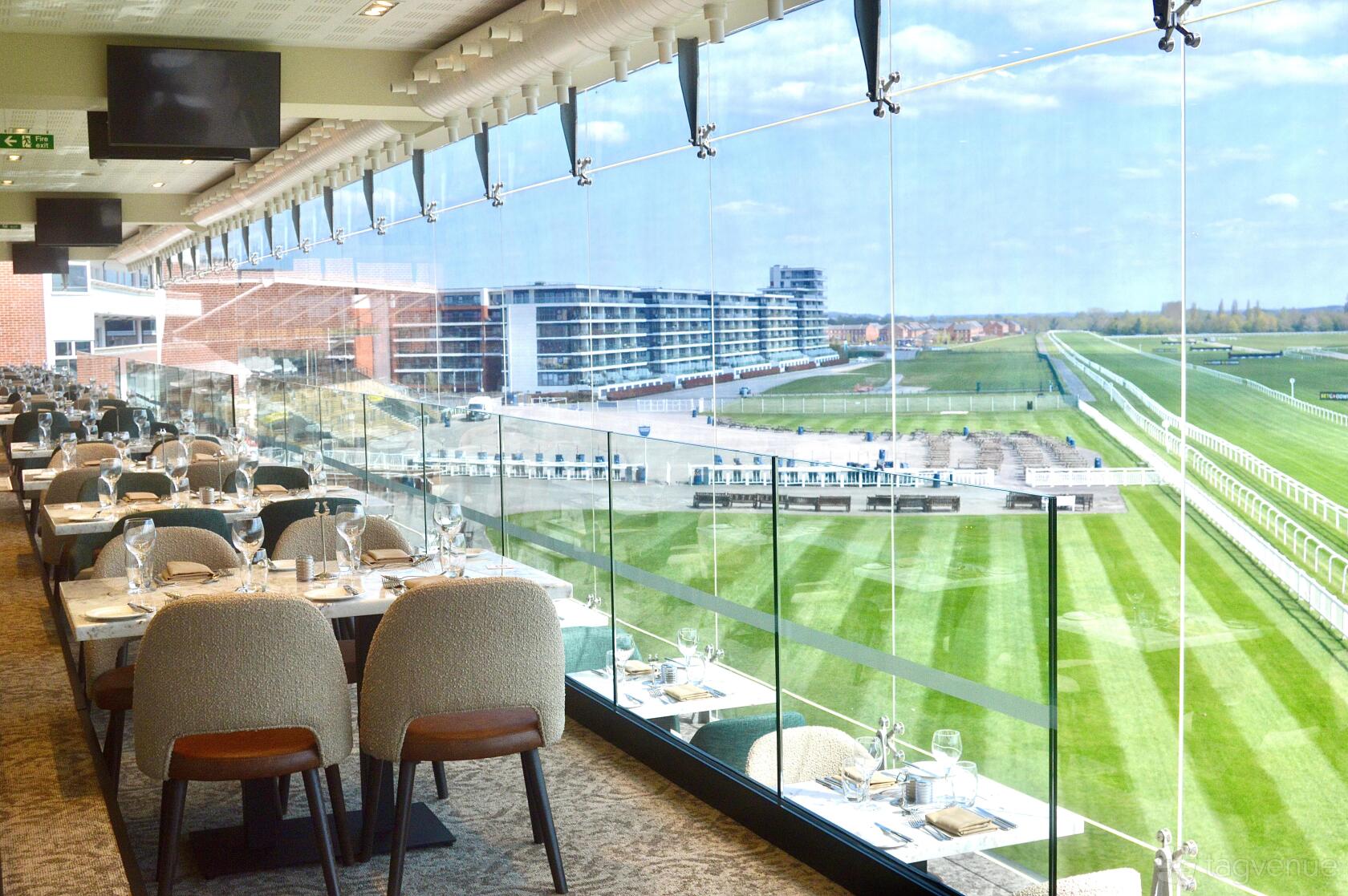 A function room with floor-to-ceiling windows overlooking the racecourse and set dining tables at Newbury Racecourse.