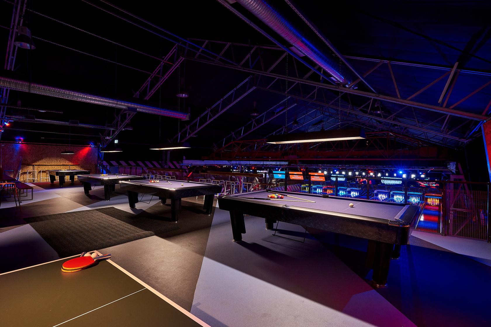 An event space with pool tables, exposed metal beams, and colorful arcade lighting at Roxy Lanes Birmingham Digbeth.