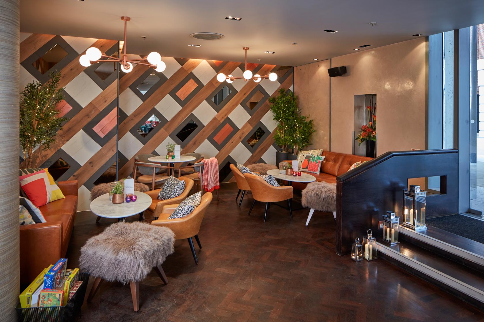 A lounge with leather chairs, fur throw stools, round marble tables, and geometric wood-panel walls at The Happenstance – Paternoster Square.